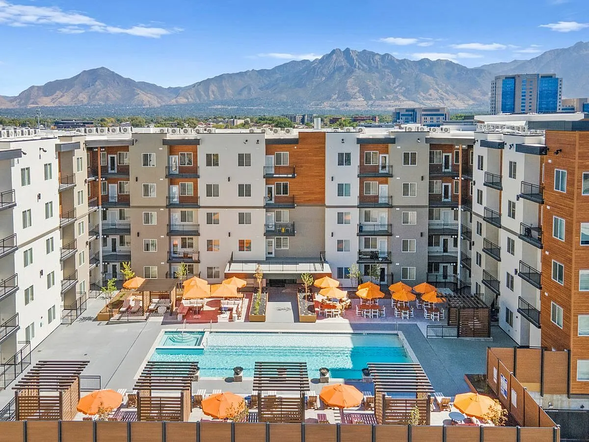 Modern apartment complex courtyard featuring inviting pool area, vibrant orange umbrellas, and stunning mountain views at Current Apartments in Murray Utah