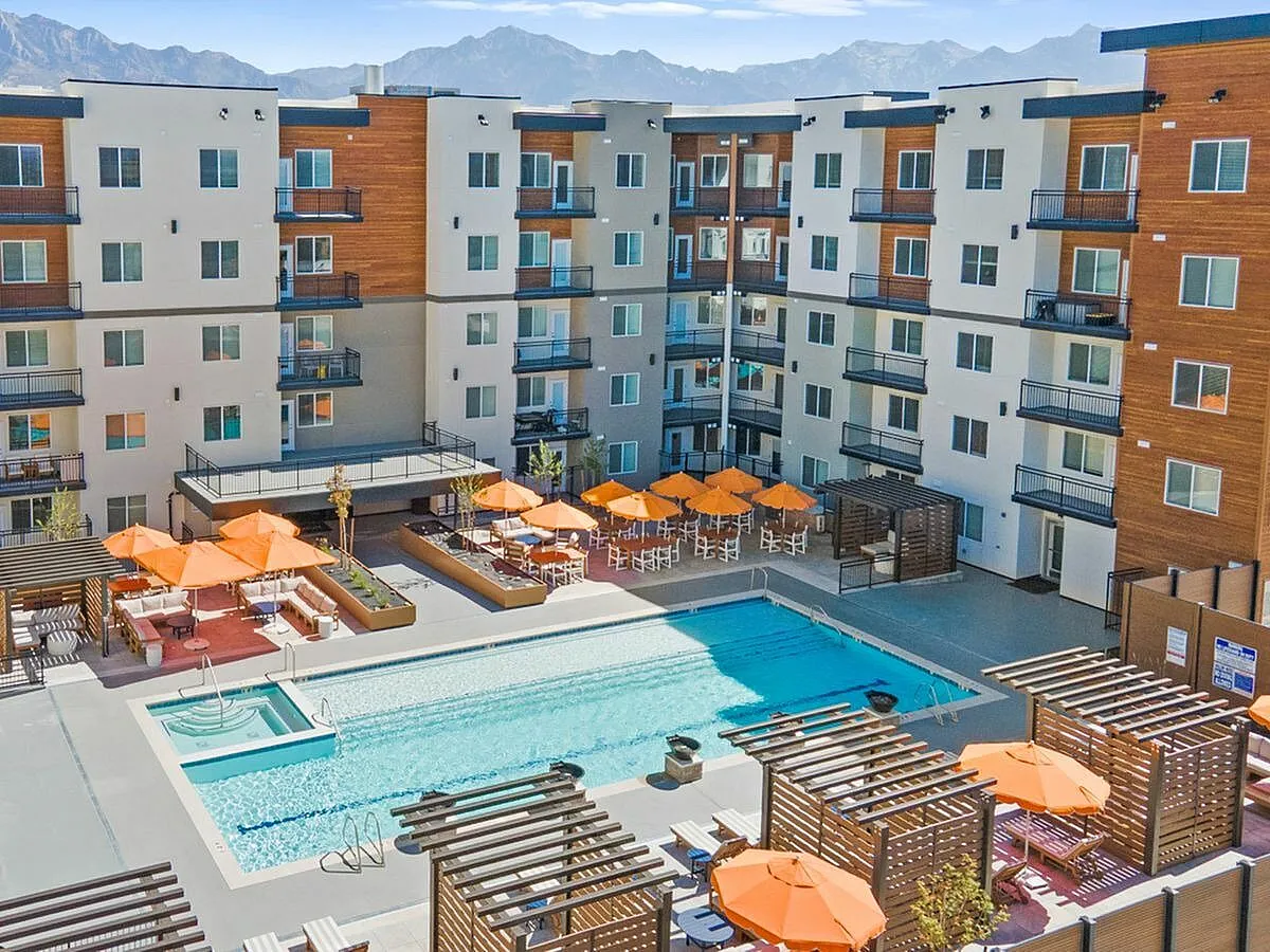Modern apartment complex featuring a spacious outdoor pool area with orange umbrellas, surrounded by scenic mountain views  at Current Apartments in Murray Utah