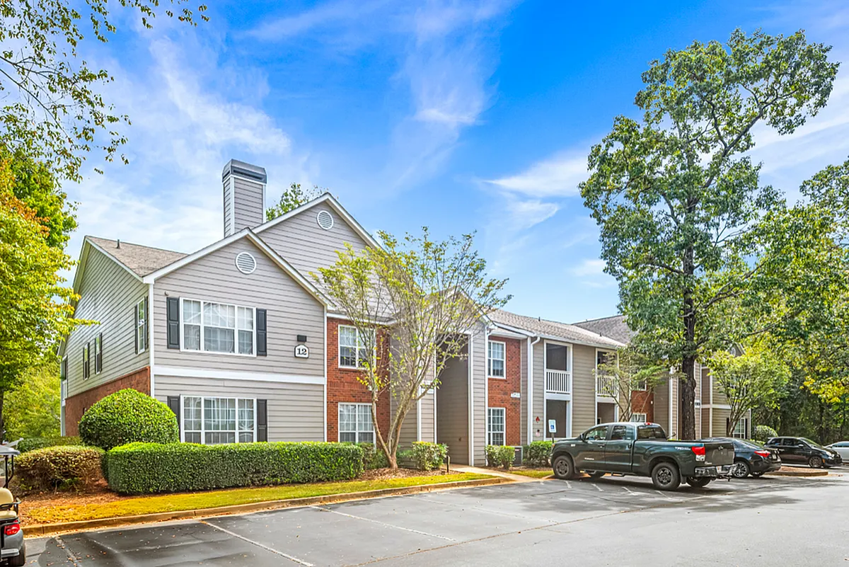 Charming apartment complex with modern architecture surrounded by lush greenery, ample parking, and vibrant skies  Retreat at Peachtree City Apartments