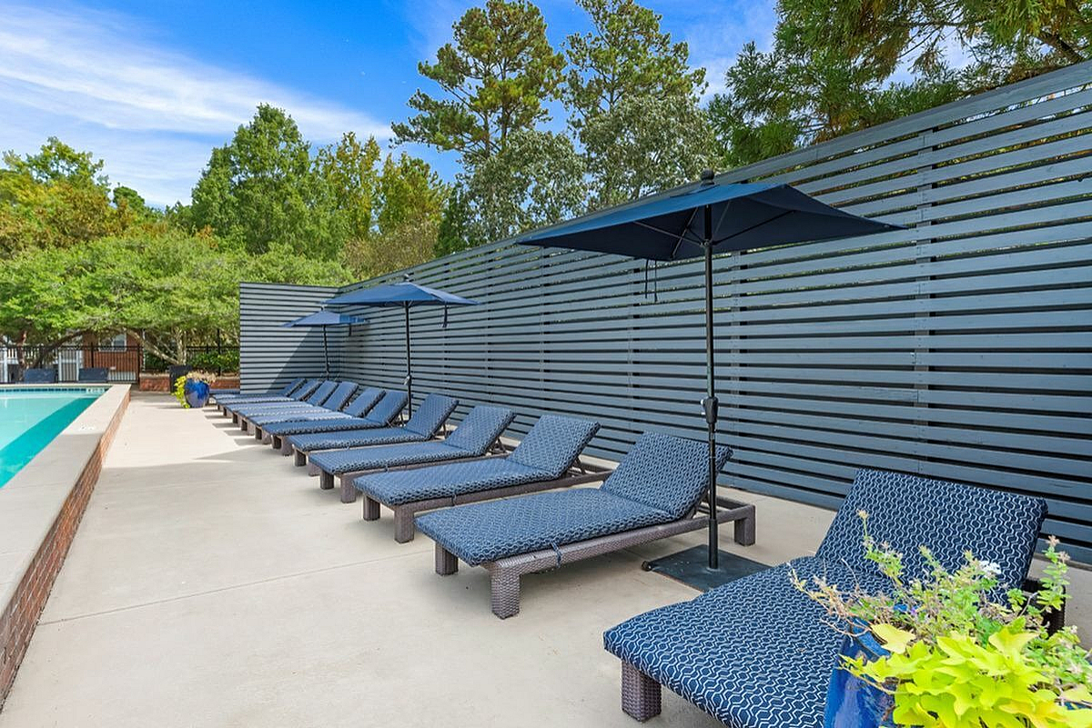 Luxurious outdoor poolside retreat featuring stylish blue loungers and elegant umbrellas, surrounded by lush greenery for a relaxing escape  Retreat at Peachtree City Apartments