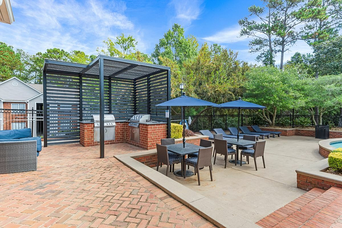 Inviting outdoor patio with shaded seating, modern grill area, and lush greenery for perfect relaxation  Retreat at Peachtree City Apartments