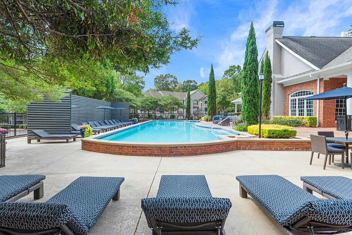 Luxurious apartment community pool area with modern lounge chairs, vibrant greenery, and inviting brick-lined pool under a blue sky  Retreat at Peachtree City Apartments