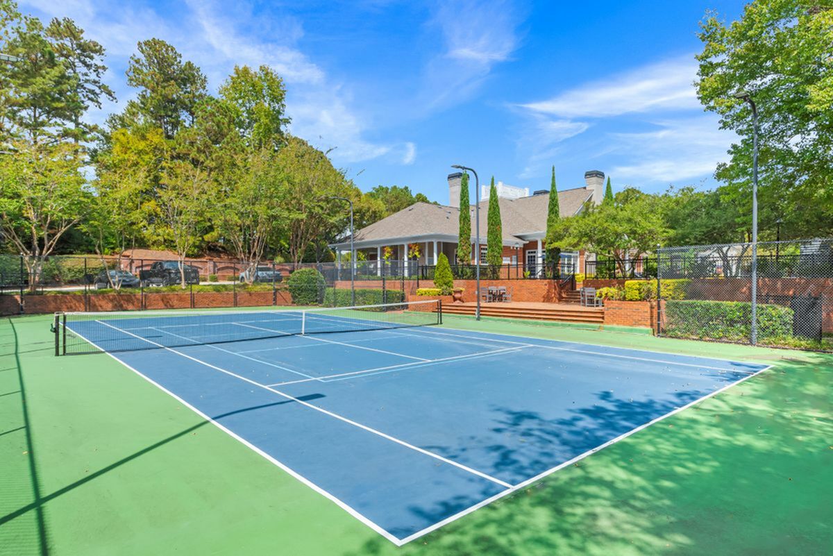 Inviting tennis court surrounded by lush greenery and charming clubhouse, perfect for outdoor recreation Enjoy the convenience of attached garages in select floor plans, offering easy access and extra storage space at Retreat at Peachtree City Apartments.