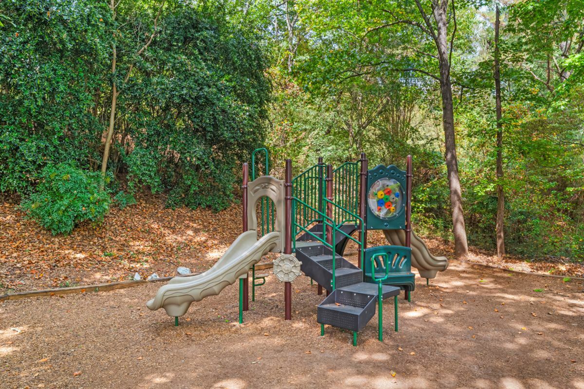 Charming outdoor playground set surrounded by lush greenery, featuring a slide and climbing structure, perfect for family fun Whether you're enjoying a match on the tennis court or strolling on the on-site walking paths, outdoor fun is always within reach at Retreat at Peachtree City Apartments in Peachtree City, GA.