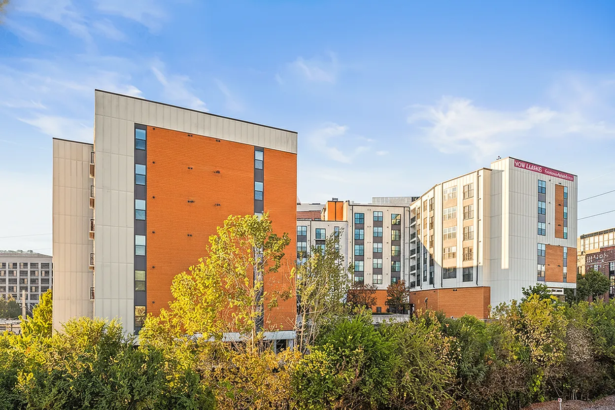 Modern apartment complex with vibrant architectural design surrounded by lush greenery against a clear blue sky.