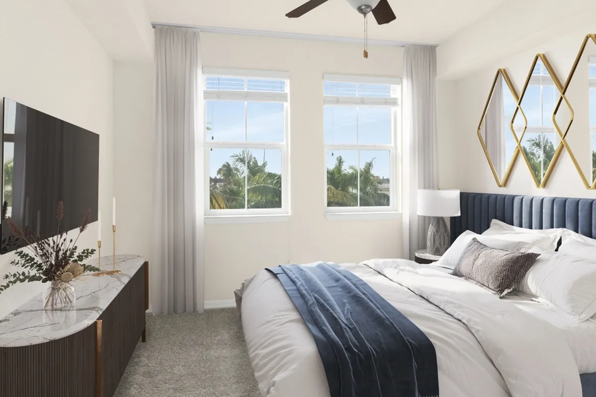 Bright and modern bedroom with plush bedding, elegant decor, and scenic views through large windows at Cottonwood Lighthouse Point Apartments in Pompano Beach