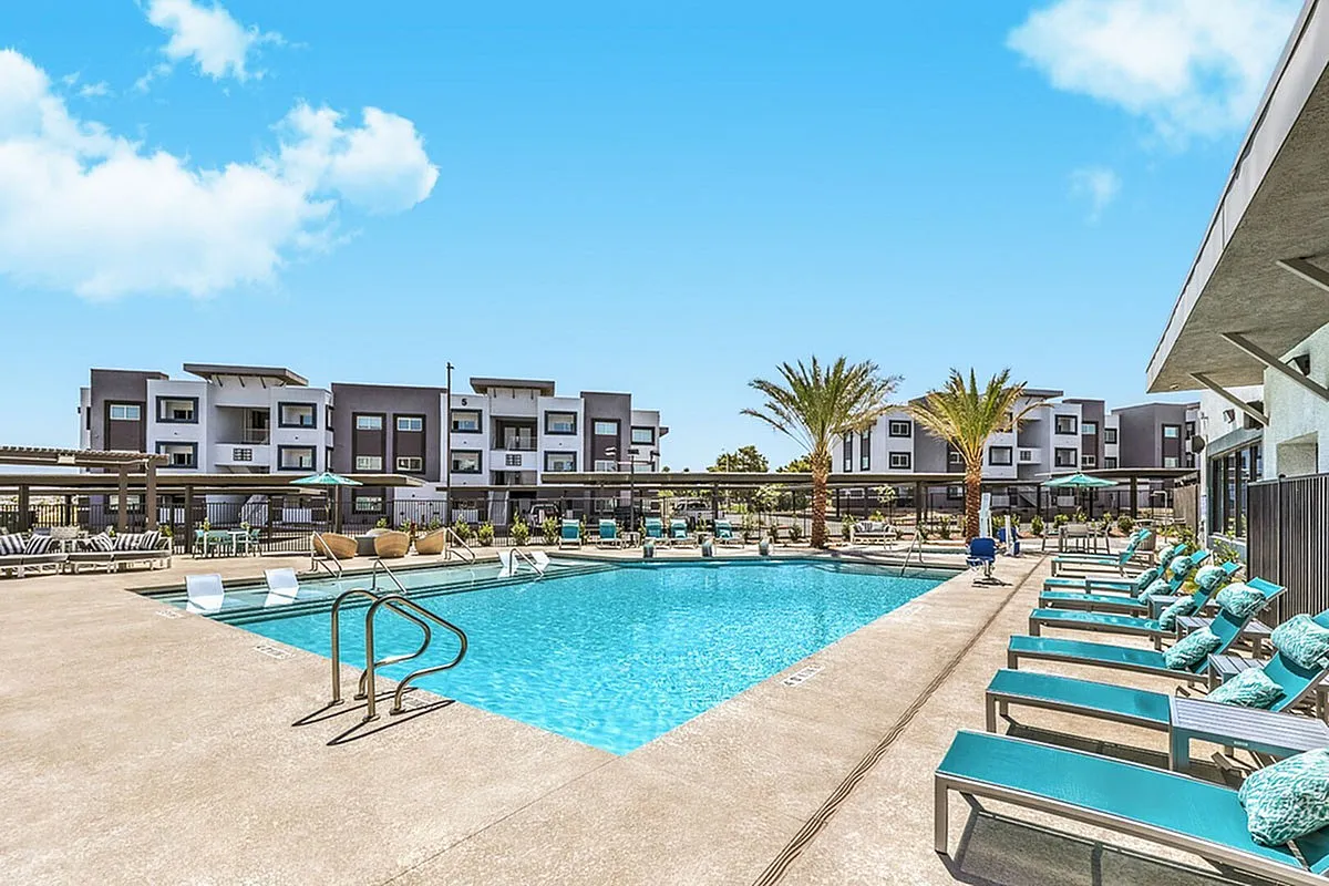 Inviting apartment complex near Las Vegas featuring a sparkling pool, modern architecture, and lush palm trees under a clear blue sky at Summit on Boulder Apartments.