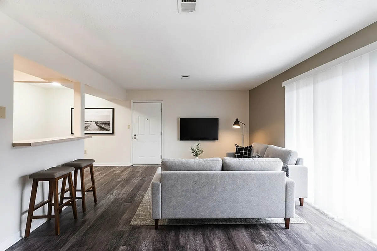 Elegant modern living room at Crown Pointe Apartments with stylish gray sofa, open-concept kitchen, and large windows for abundant natural light.