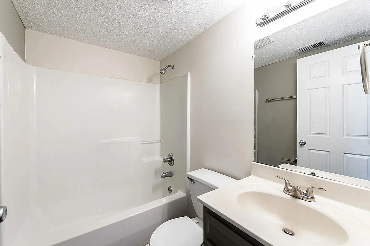 Modern bathroom at Crown Pointe Apartments with sleek white fixtures, a full bathtub, and an elegant sink with a large mirror, offering a fresh and inviting atmosphere.