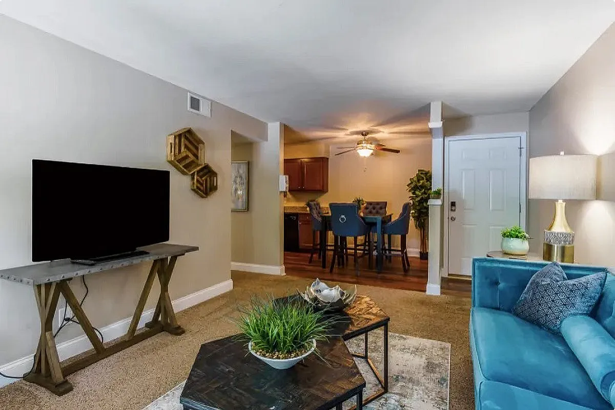 Chic apartment living space at The Creeks on Kirklevington Apartments featuring a modern open-plan design with a cozy blue sofa, stylish wall decor, elegant lighting, and an inviting dining area in the background.