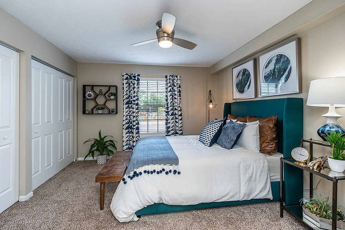 Charming bedroom at The Colony at the Oaks Apartments with cozy decor, featuring a plush bed, stylish blue accents, and warm natural light.