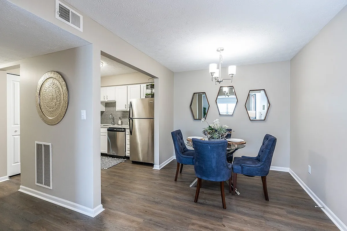 Elegant dining area at The Colony at the Oaks Apartments with stylish blue chairs, mirrored accents, and a modern kitchen view with stainless steel appliances.