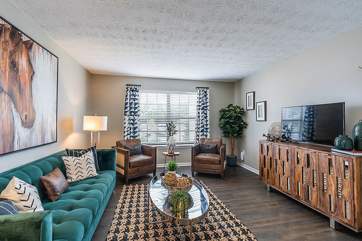Modern living room at The Colony at the Oaks Apartments with elegant decor, featuring a vibrant emerald sofa, stylish wooden furniture, and eye-catching geometric curtains.