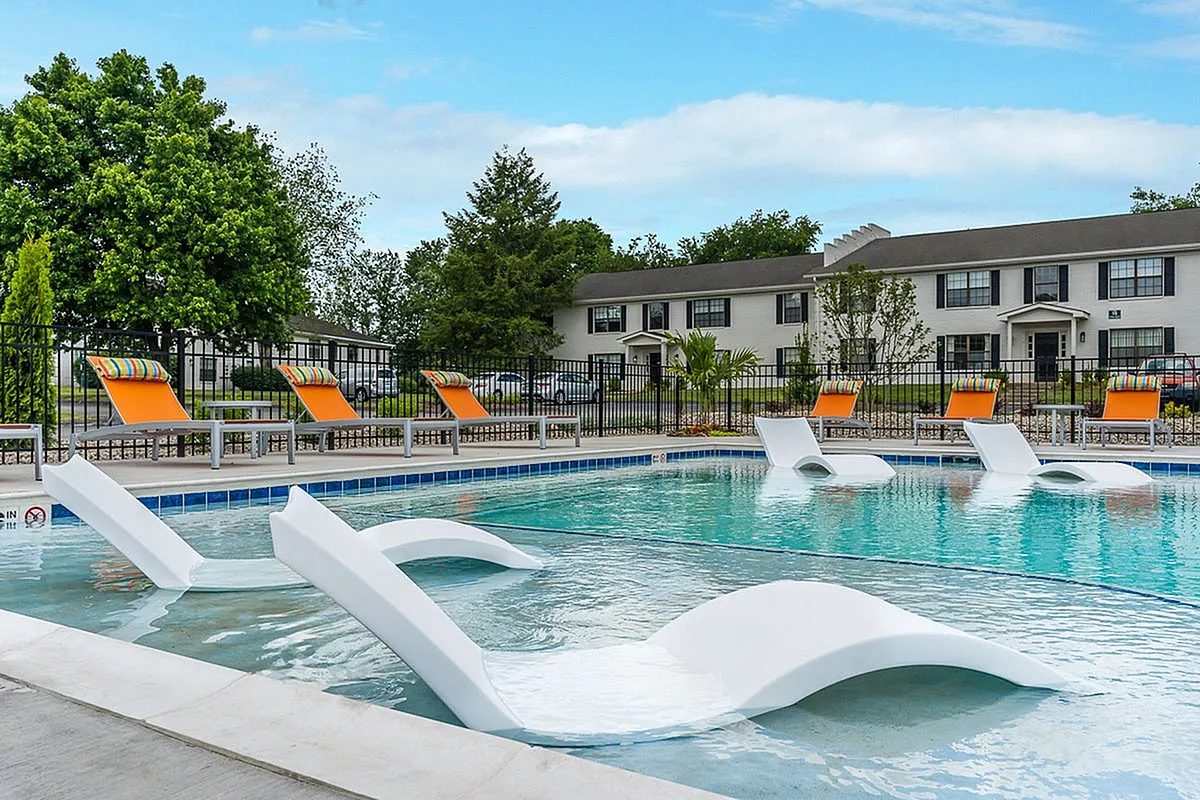 Inviting pool area at The Colony at the Oaks Apartments with stylish lounge chairs, surrounded by lush greenery and modern architecture.