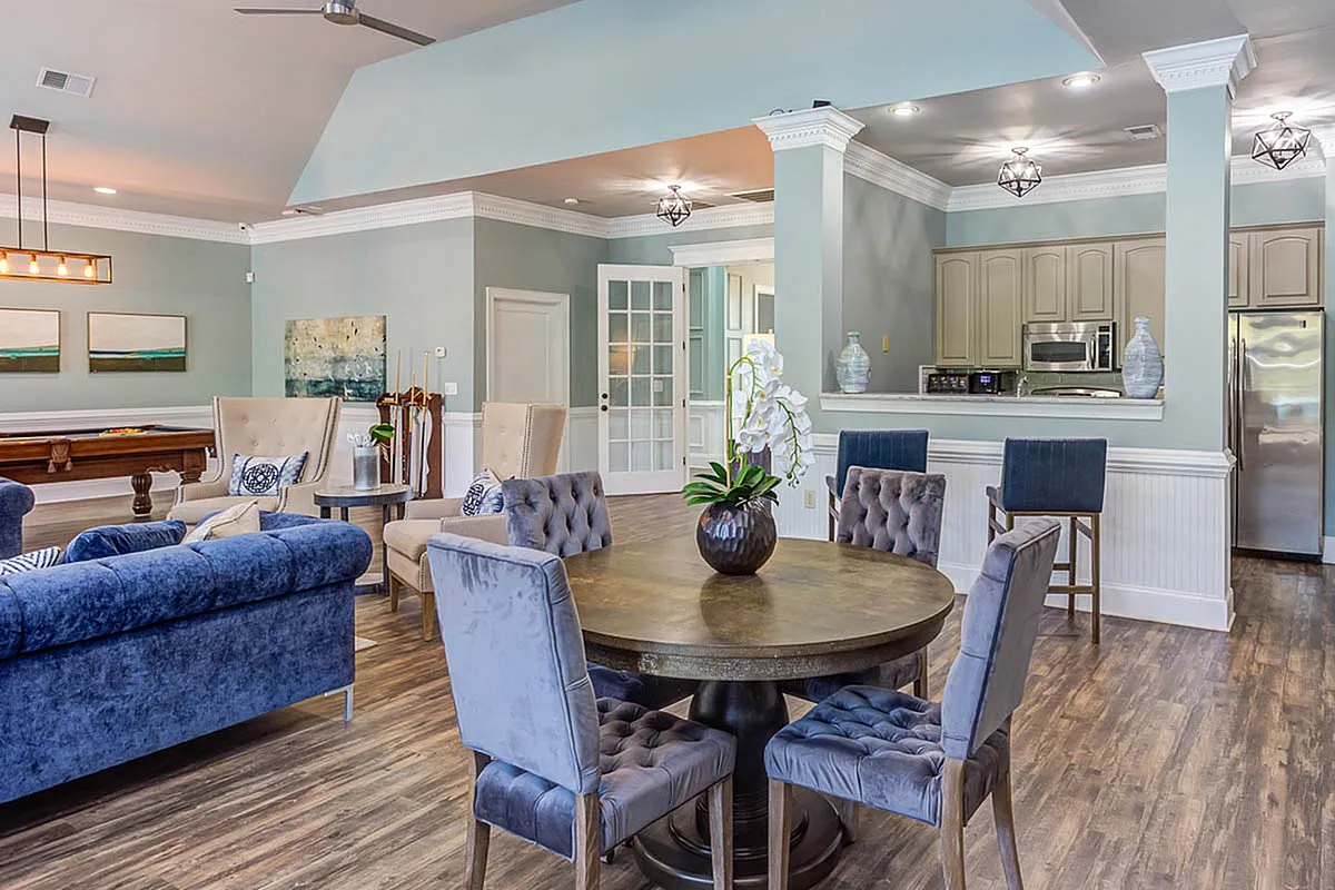 Elegant clubroom at The Stratford at Hillcrest Towne Center Apartments featuring a stylish dining area with plush velvet chairs, a chic lounge, and a modern kitchen with stainless steel appliances.