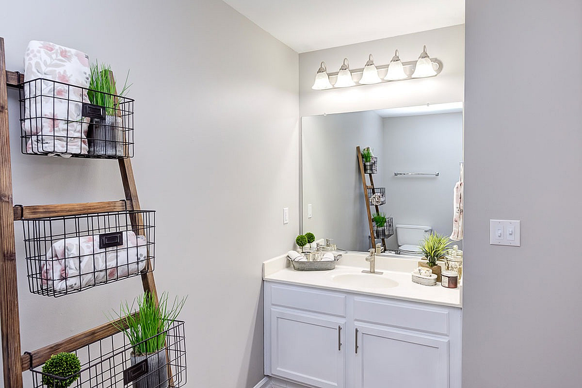 Contemporary bathroom at The Stratford at Hillcrest Towne Center Apartments with elegant countertop, stylish lighting, and a chic ladder shelf for storage.