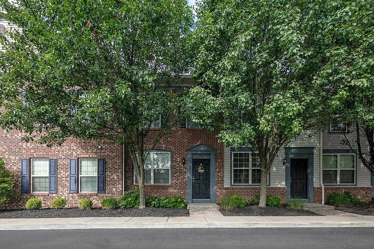 Charming brick townhouse with elegant blue shutters, large windows, and lush greenery, offering an inviting curb appeal at The Mill at Georgetown Apartments.
