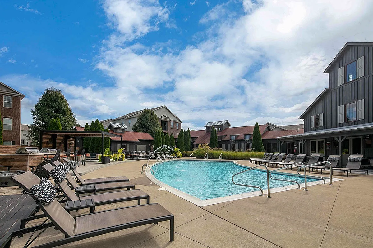 Charming residential complex with inviting outdoor pool, stylish lounge chairs, lush landscaping, and clear blue skies, offering a perfect retreat for relaxation at The Mill at Georgetown Apartments.