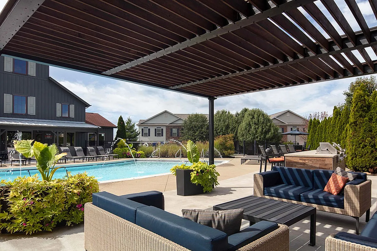 Inviting outdoor patio at The Mill at Georgetown Apartments featuring cozy seating under a stylish pergola, with views of a sparkling pool and manicured garden.