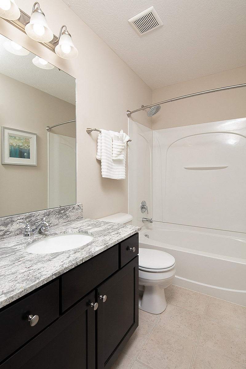 Elegant bathroom at The Mill at Georgetown Apartments featuring a sleek granite countertop, modern vanity, and pristine white bathtub with stylish lighting.