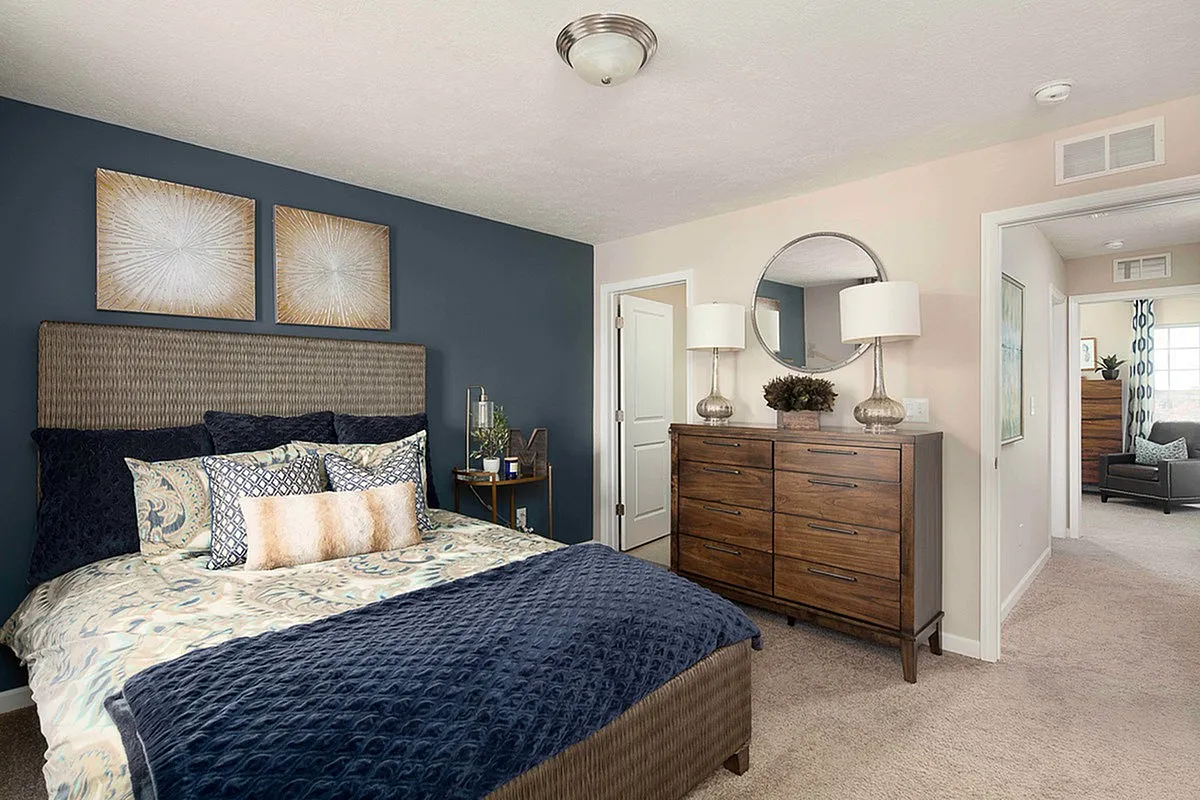 Inviting bedroom with plush bedding, rich blue accent wall, and elegant wooden furniture, creating a cozy and stylish retreat at The Mill at Georgetown Apartments.