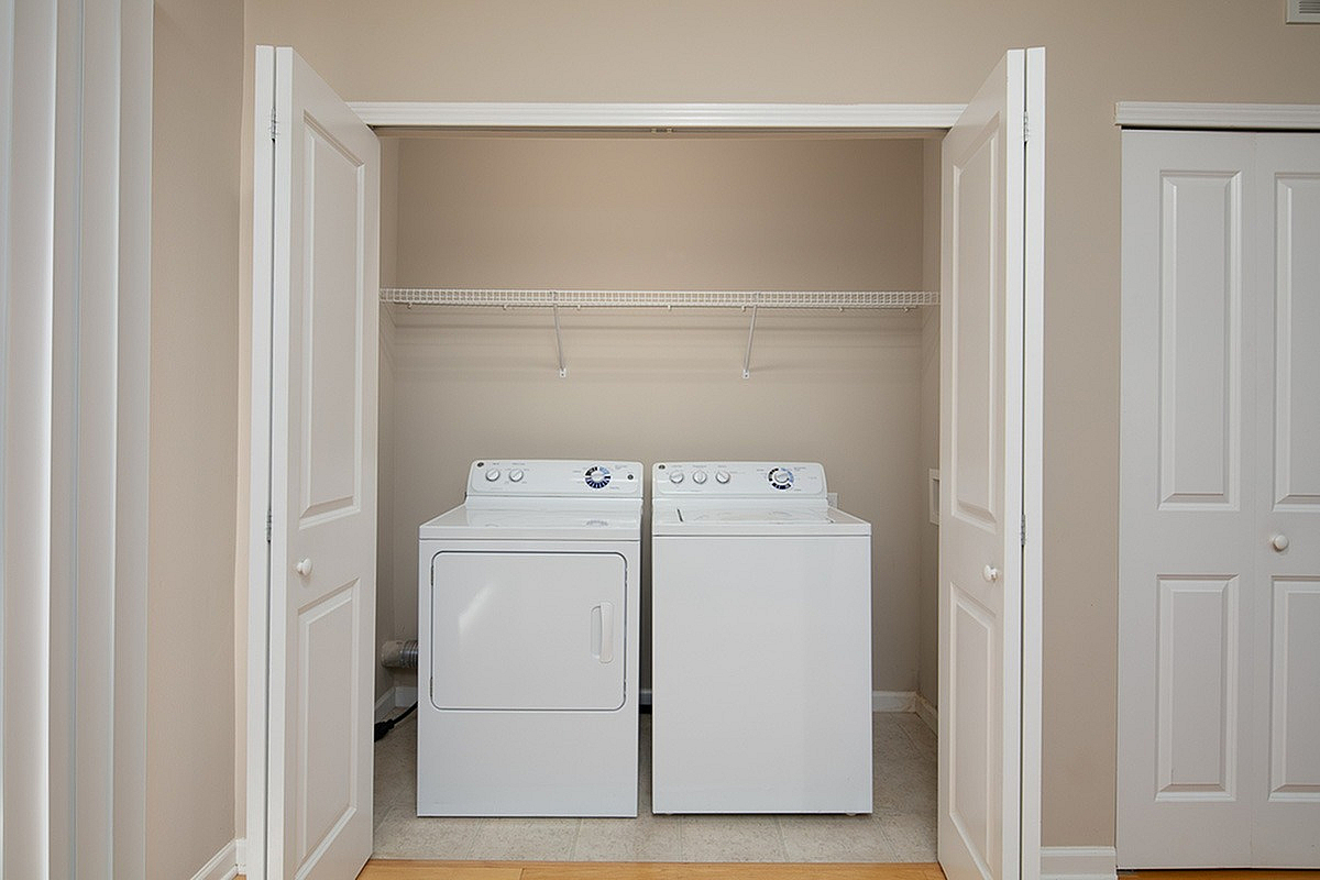 Modern laundry area at The Mill at Georgetown Apartments equipped with a washer and dryer, featuring spacious white cabinetry and a sleek design.
