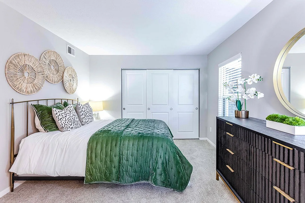 Bright and elegant bedroom at The Retreat at Stillmeadow Apartments featuring a cozy bed with green accents, stylish wall decor, and a sleek dresser with modern design touches.