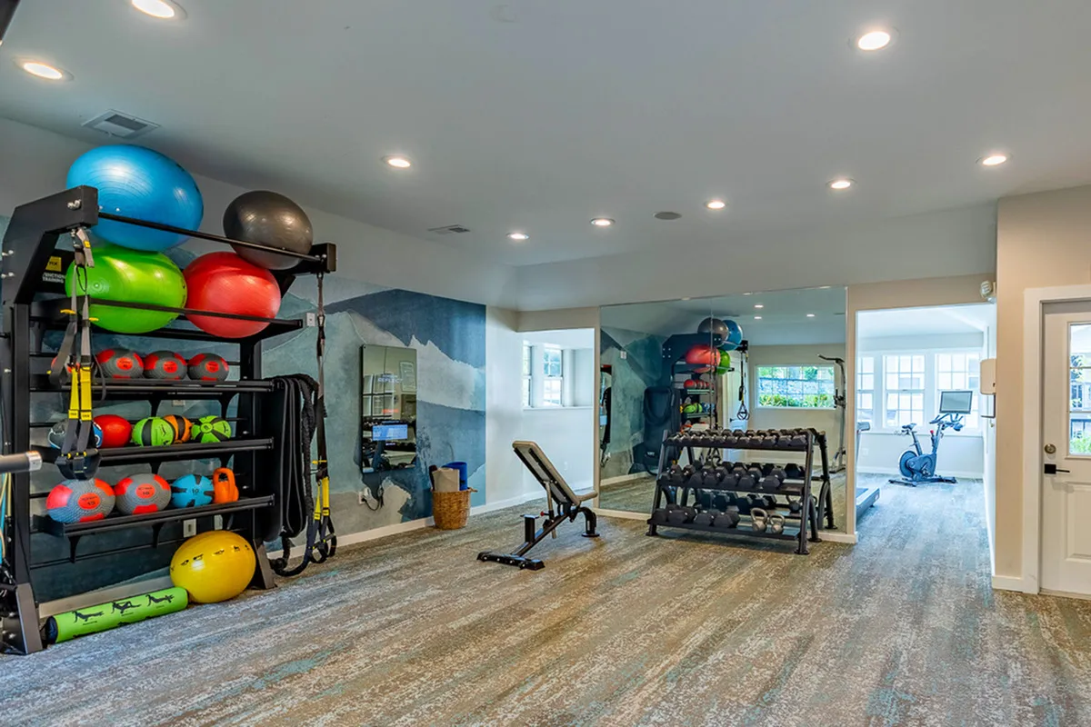 Modern fitness room at The Retreat at Stillmeadow Apartments with vibrant exercise equipment, weights, and a mirrored wall, offering a motivational gym environment.
