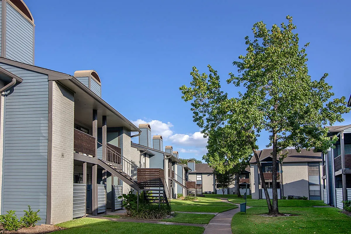 Charming apartment complex, Steepleway Downs Apartments, with modern architecture, lush green lawns, and abundant trees under a clear blue sky.