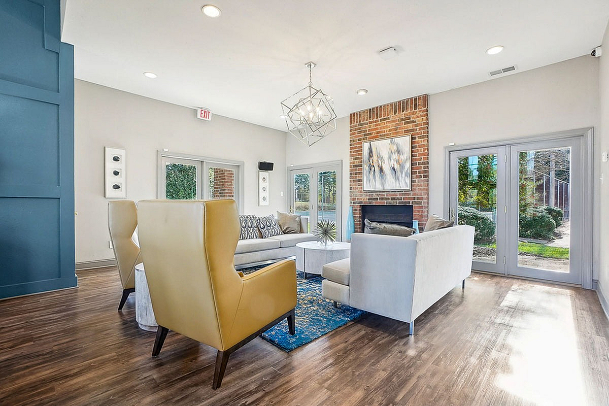 Elegant clubroom at Park at Midtown Apartments featuring modern furniture, a brick fireplace, and floor-to-ceiling windows opening to a scenic view.