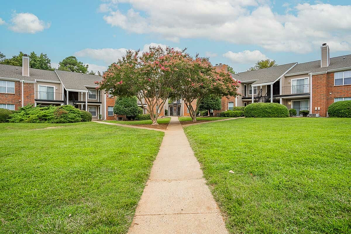 Charming apartment complex, Park at Midtown Apartments, with manicured lawns, beautiful trees, and brick architecture under a bright blue sky.