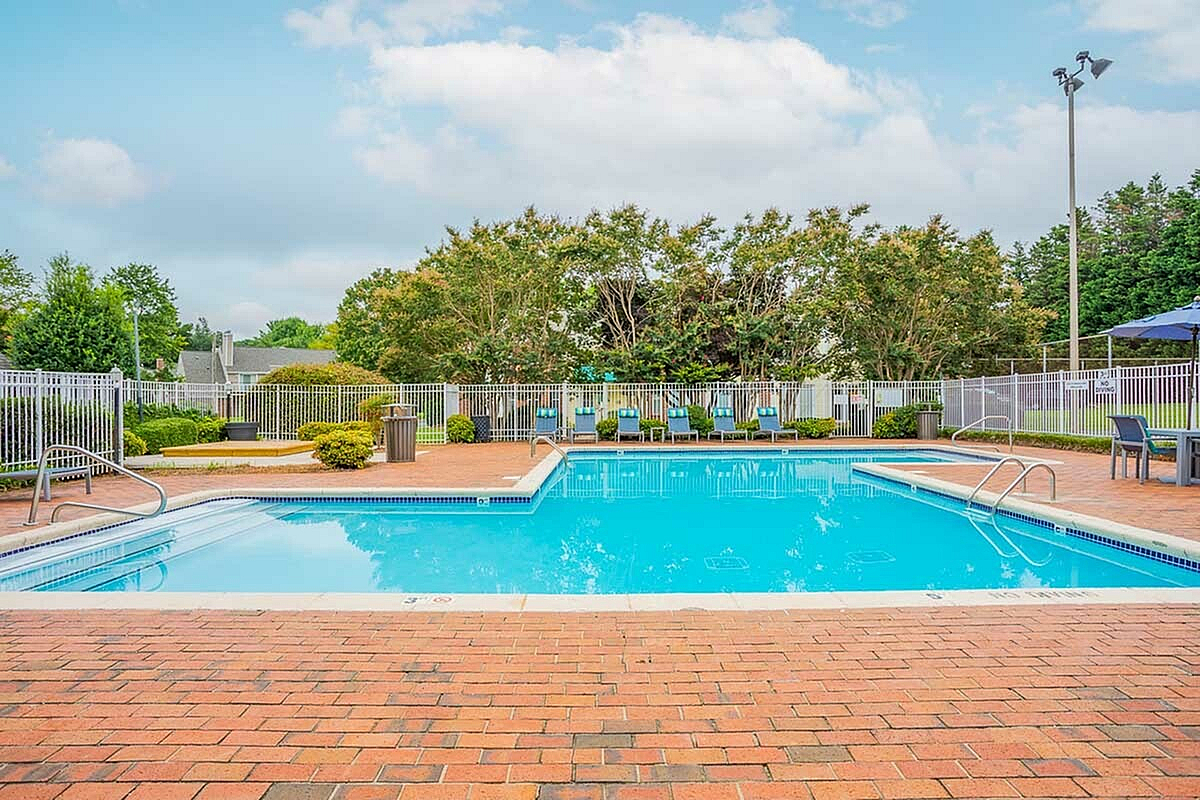 Inviting outdoor pool area at Park at Midtown Apartments with comfortable lounge chairs, surrounded by lush greenery and clear blue skies.