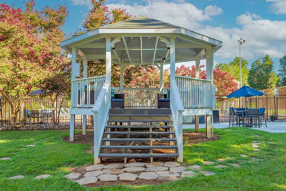 Charming outdoor gazebo at Park at Midtown Apartments with elegant white railings, surrounded by lush greenery and vibrant flowers, ideal for relaxation and gatherings.