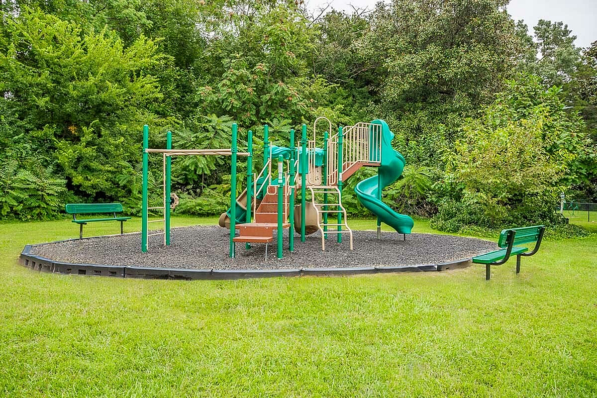 Charming playground set at Park at Midtown Apartments with vibrant green slides and climbing equipment, surrounded by lush greenery and inviting benches.