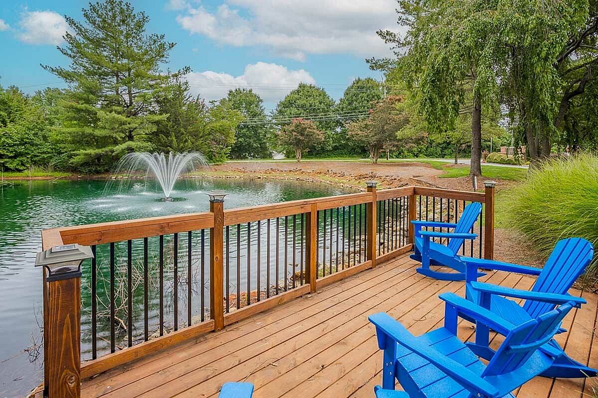 Charming outdoor deck at Park at Midtown Apartments with vibrant blue chairs overlooking a serene pond and fountain, surrounded by lush greenery.