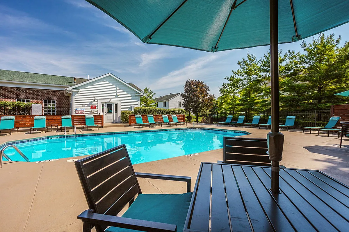 Inviting outdoor swimming pool area at Alkire Glen Apartments with modern patio seating, surrounded by lush greenery and clear blue skies.