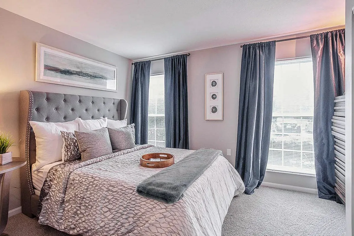 Elegant bedroom at Alkire Glen Apartments with plush bedding, stylish gray curtains, and chic decor in a bright, inviting space.