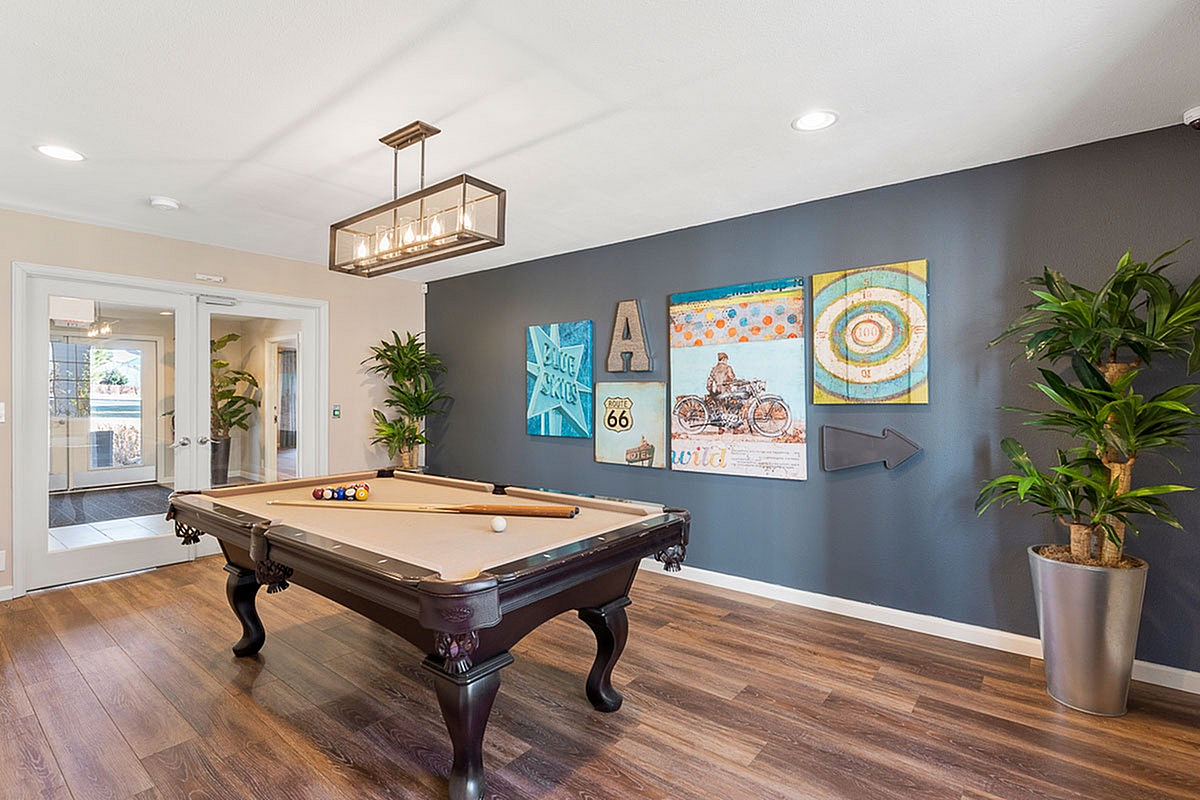 Inviting recreational room at Antero Apartments with stylish pool table, vibrant wall art, and elegant wood flooring.