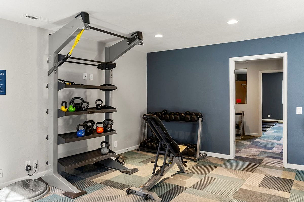 Bright and modern fitness room featuring a versatile weight rack, colorful kettlebells, and an adjustable bench, perfect for an energizing workout at Antero Apartments in Colorado Springs