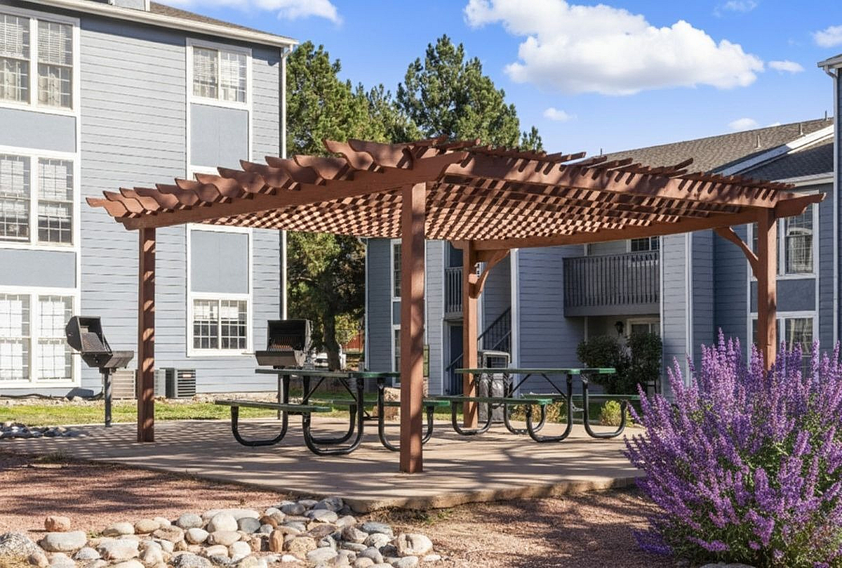 Beautiful outdoor living space featuring a wooden pergola, picnic tables, and lush landscaping in a serene apartment complex at Antero Apartments in Colorado Springs.