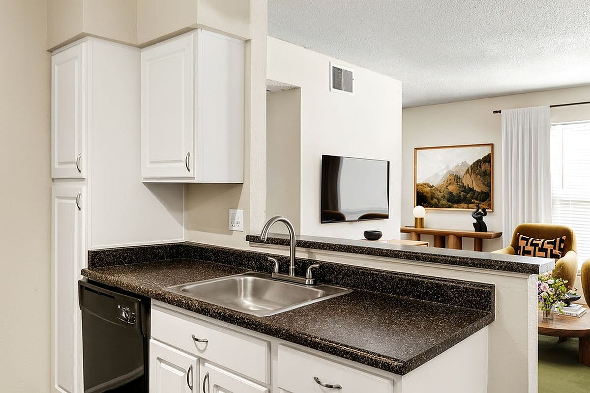 Bright and modern kitchen with sleek countertops, open view to stylish living area featuring wall-mounted TV and chic decor at Antero Apartments in Colorado Springs.