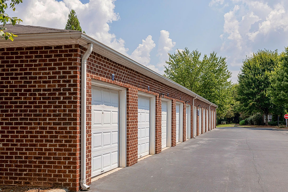 Charming brick garages at Morgan Ridge Apartments with white doors in a tranquil residential area, surrounded by lush greenery and a clear blue sky.