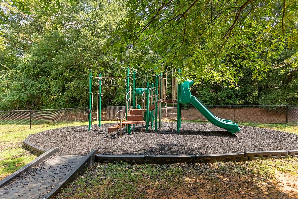 Charming outdoor playground with vibrant green slides and climbing structures, surrounded by lush trees, perfect for family enjoyment at Morgan Ridge Apartments.