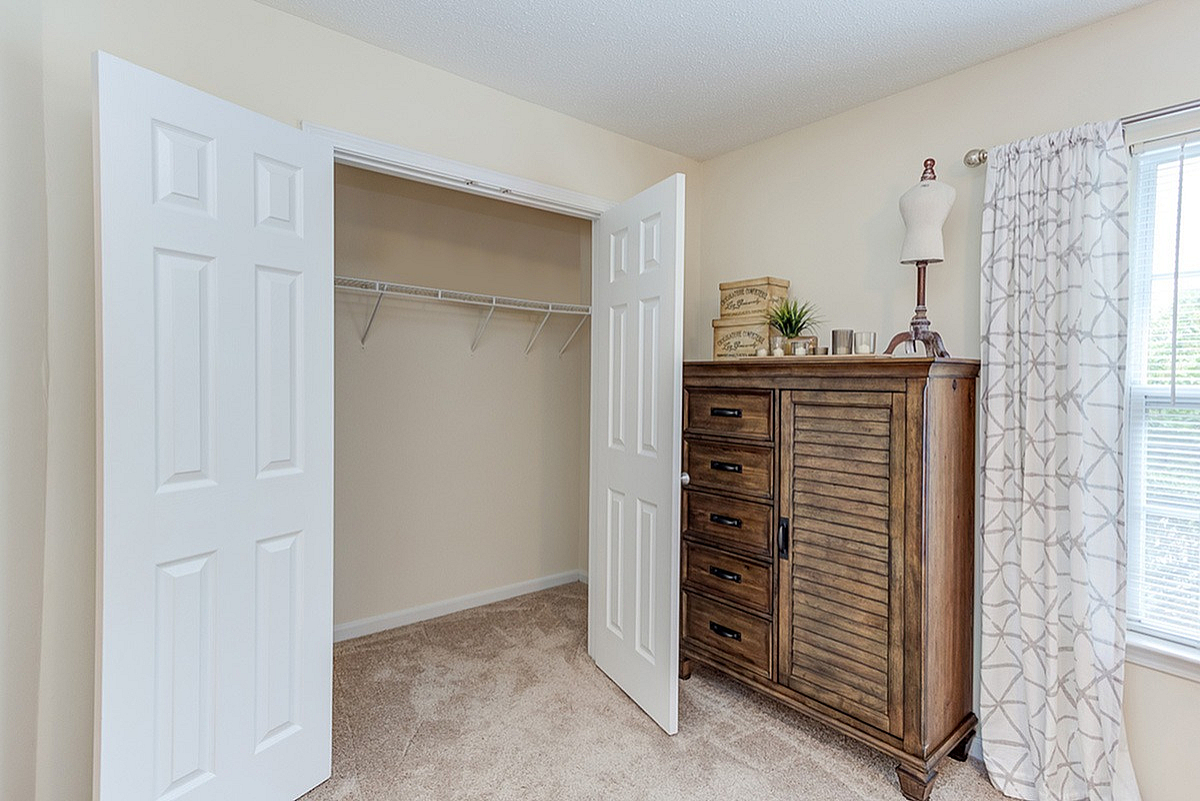 Cozy bedroom at Morgan Ridge Apartments with elegant wooden dresser, open closet space, and large window providing ample natural light.