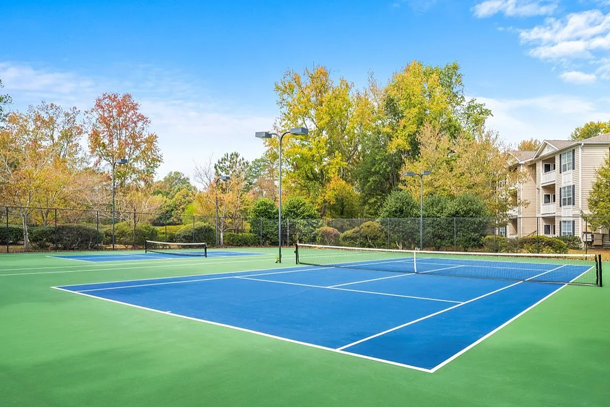 Inviting tennis court surrounded by lush greenery and modern apartments, perfect for outdoor activities and relaxation at Lake St James Apartments in Conyers GA.