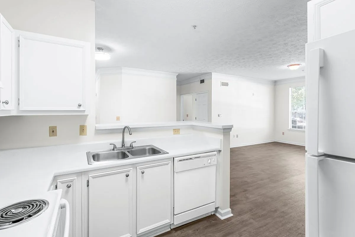 Bright open-concept kitchen with modern white cabinetry, sleek countertops, and a spacious living area, perfect for entertaining  at Lake St James Apartments.