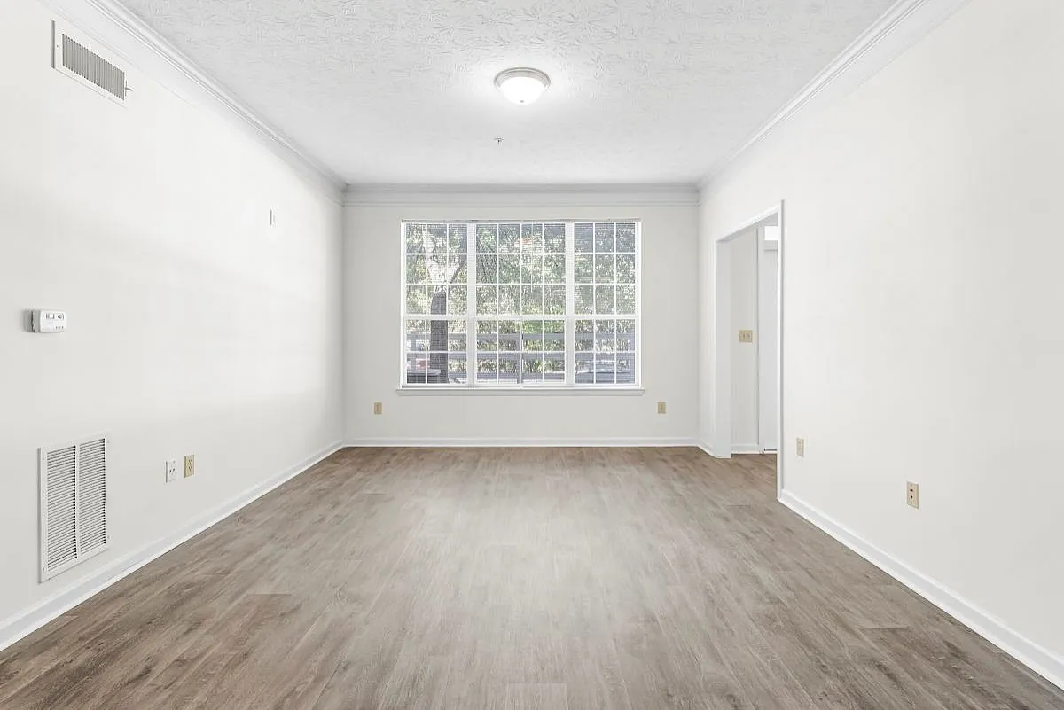 Bright and airy living room with elegant wood flooring and a large window offering a serene outdoor view  at Lake St James Apartments.