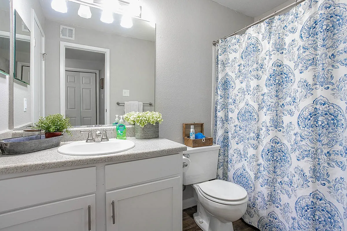 Bright and elegant bathroom at Autumn Ridge Apartments featuring a modern white vanity, vibrant floral shower curtain, and stylish countertop accents.