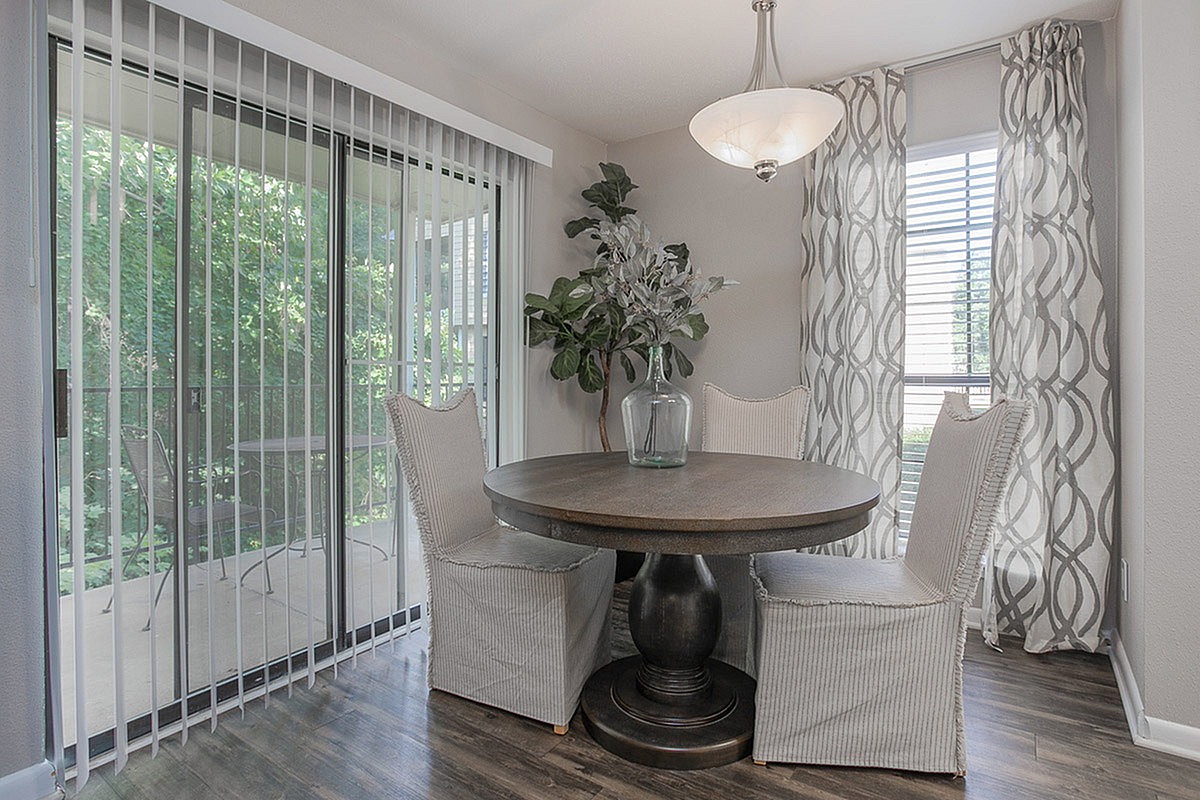Charming dining area at Autumn Ridge Apartments with elegant round table, surrounded by soft chairs and natural light through glass sliding doors and stylish curtains.