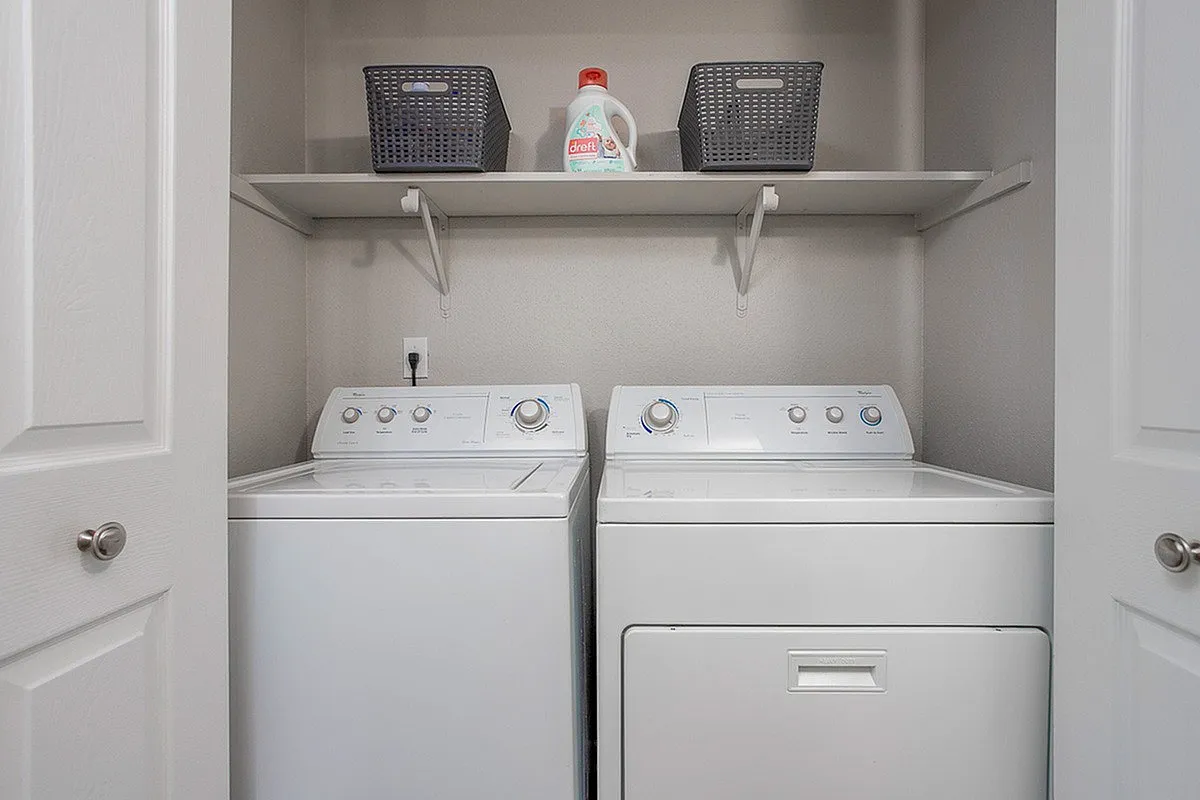 Modern laundry room at Autumn Ridge Apartments with sleek washer and dryer, enhancing convenience with stylish storage baskets on a shelf above.